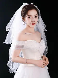 Detail view of a short white bridal veil featuring elegant pearl embellishments on a model