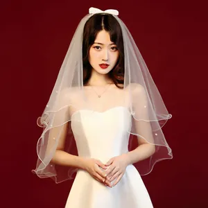 Detailed view of a short white bridal veil featuring pearl accents and a dainty bow