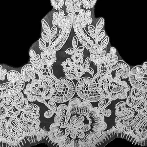 Dettaglio macro del pizzo ricamato floreale bianco con paillettes su rete per cucito fai-da-te