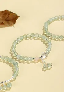Macro detail of prehnite beaded bracelet with crystal butterfly and rose quartz accents.