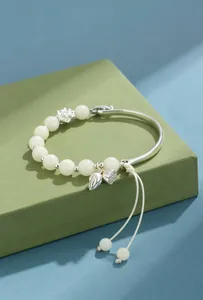 Vista detallada de pulsera de cuentas de Bodhi blancas con dijes de loto de plata y cordón