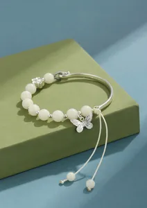 Detalle de pulsera de cuentas de Bodhi blanca con colgante de mariposa y parte metálica