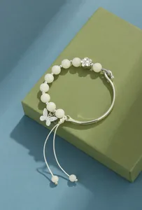 Detalle de una pulsera de cuentas de bodhi blanca con dijes de mariposa y flor de metal.