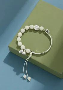 Vista macro de cuentas de bodhi blancas y dijes de loto en un brazalete rígido de plata