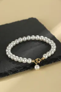 Elegant white faux pearl bracelet featuring a gold-plated clasp and a delicate hanging pearl charm detail.