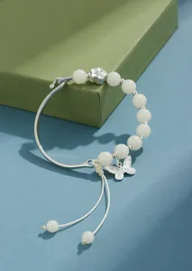 Vista detallada de pulsera de cuentas Bodhi blanca con dije de mariposa de plata y flor.