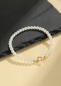 Close-up detail of a minimalist white pearl bracelet with a golden spring ring clasp.