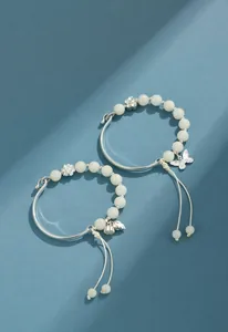 Vista detallada de pulseras de cuentas de Bodhi blancas con dijes de flores y mariposas plateadas