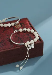 Detalle de pulsera de semillas de bodhi blancas con dije de mariposa plateada en caja roja