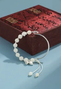 Detalle de pulsera de bodhi blanca con dijes de loto y caja de regalo roja elegante
