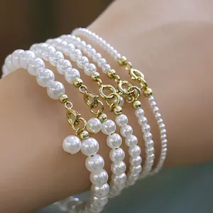 Detailed view of layered white faux pearl bracelets with gold lobster clasps on a wrist.
