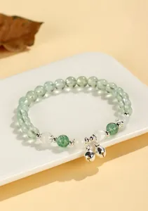 Detail shot of green prehnite beaded bracelet with two silver bell charms on white plate