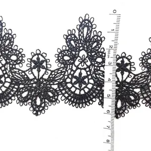 Detailed view of black water-soluble openwork lace trim showing width with measuring tape