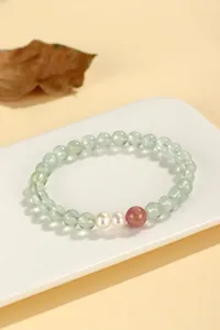 Macro view of prehnite and pearl beaded bracelet on a white porcelain display tray