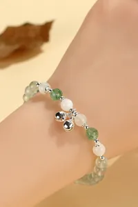 Close-up of a beaded bracelet with green and white gemstones and silver bell charms on wrist