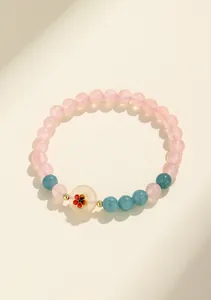 Primo piano di bracciale con perline di quarzo rosa e agata blu con ciondolo a fiore rosso.