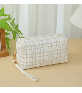 Detailed view of white and gold tweed cosmetic bag with elegant gold zipper and wrist strap
