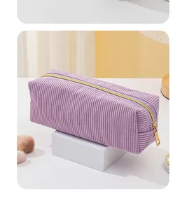 Detailaufnahme einer lila Cord-Kosmetiktasche mit goldenem Reißverschluss auf Podest.
