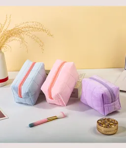 Detailweergave van pastelkleurige pluche make-uptassen met geborduurd ruitpatroon.