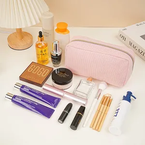 Large pink corduroy cosmetic bag surrounded by various makeup products on a cream desk