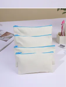 Detail view of a stack of four blank canvas pouches with blue zippers on a white desk