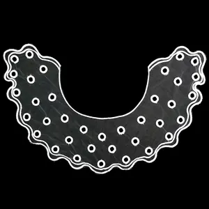 Close-up view of a white embroidered organza lace collar with wavy edges and round cutouts.