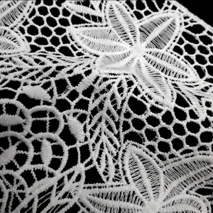 Macro detail of white water-soluble lace flower with intricate embroidery.