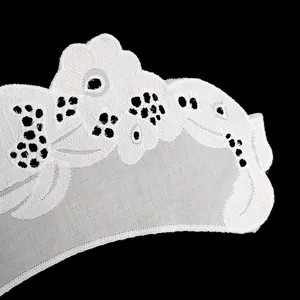 Macro detail of delicate white cotton eyelet embroidery lace trim on a black background.