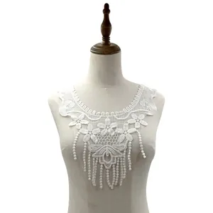 Detalle de cuello de encaje blanco soluble en agua con diseño floral y flecos colgantes
