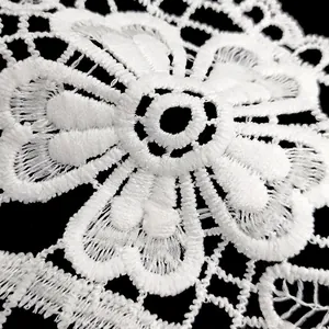 Macro detail of white milk silk water-soluble lace embroidery with hollow flower pattern.