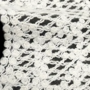 Macro view of white embroidered floral lace fabric with delicate rose patterns and mesh backing