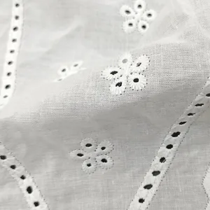 Close-up of white cotton fabric with delicate floral eyelet embroidery and cutout detail