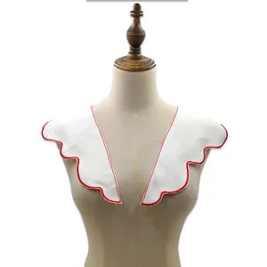 Detailed view of a white embroidered detachable collar with red scalloped edges on a mannequin