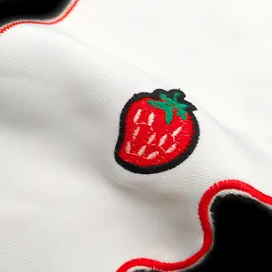 Macro view of detailed strawberry embroidery on white fabric with red scalloped edge