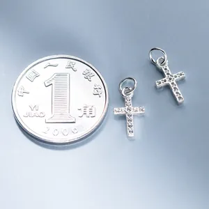 Nahaufnahme eines kleinen Kreuzanhängers aus 925er Silber mit funkelnden Steinen und Münze