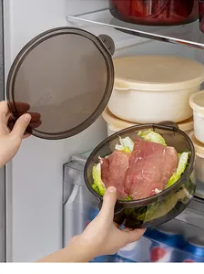Hand holding a transparent dark grey food storage bowl with lid inside a refrigerator