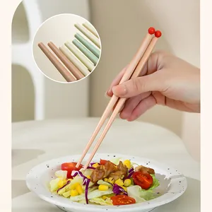 Close-up of pastel dopamine color chopsticks with red ball tips using on salad bowl