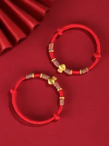 Détail de deux bracelets tressés rouges avec des breloques serpent porte-bonheur dorées