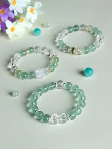 Detailed view of green fluorite and white crystal beaded bracelets with bow and Pixiu charms.
