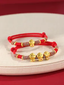 Détail de bracelets tressés rouges avec des breloques serpent en or pour l'année du Serpent