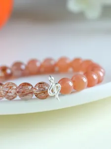 Detailed view of a 925 silver snake charm on a sunstone and super seven beaded bracelet