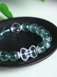 Close-up of green fluorite and clear quartz bow beaded bracelet on a ceramic dish