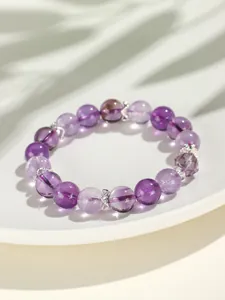 Detailopname van een amethist kralenarmband op een wit bord met schaduwen van bladeren.