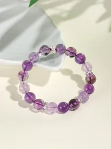 Detailopname van een lavendel amethist kralenarmband met zilveren bloemenbedels op plateau