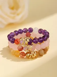 Detail view of crystal beaded bracelets featuring golden snake charms in amethyst and quartz.