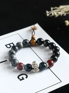 Macro detail of 999 silver snake charm on a beaded bracelet with onyx and tiger eye stones.