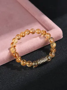 Detalle de pulsera de cuentas de cristal amarillo con un tubo de metal dorado martillado.
