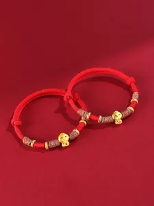Gros plan de bracelets tressés rouges avec des breloques serpent dorées porte-bonheur.