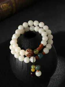 Makro-Detail eines zweischleifigen weißen Bodhi-Samen-Armbands auf einer schwarzen Ziervase