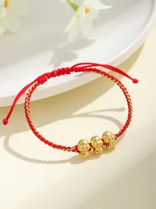 Dettaglio di tre ciondoli a forma di serpente dorati su bracciale rosso